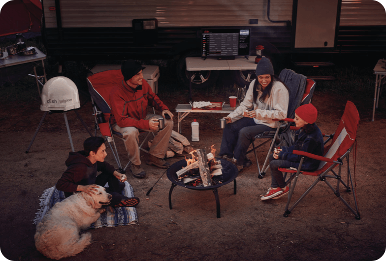 Family sitting around a fire , camping with a television on behind them on top of a table.